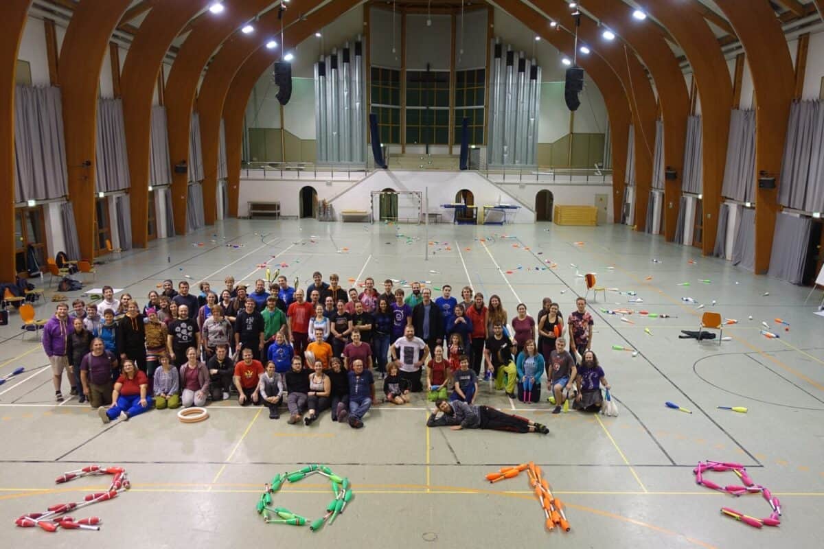 Large group photo at PassOut Krelingen event in a gymnasium, juggling clubs scattered on the floor forming "2018". - Passing Zone