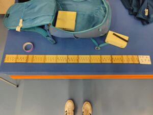 Measuring tape with numbers, backpack, and feet on a blue surface. - Passing Zone
