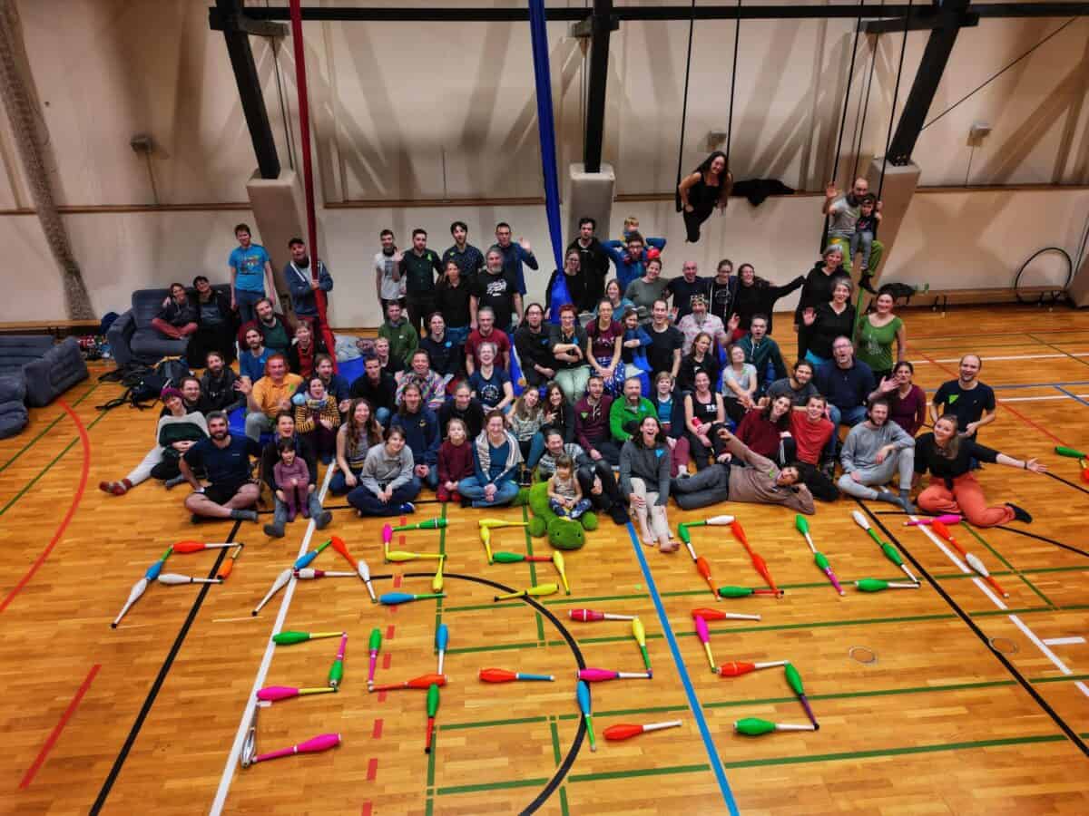 Large group photo at PassOut Dreiskau-Muckern event, people sitting and standing, juggling clubs spelling "PassOut". - Passing Zone
