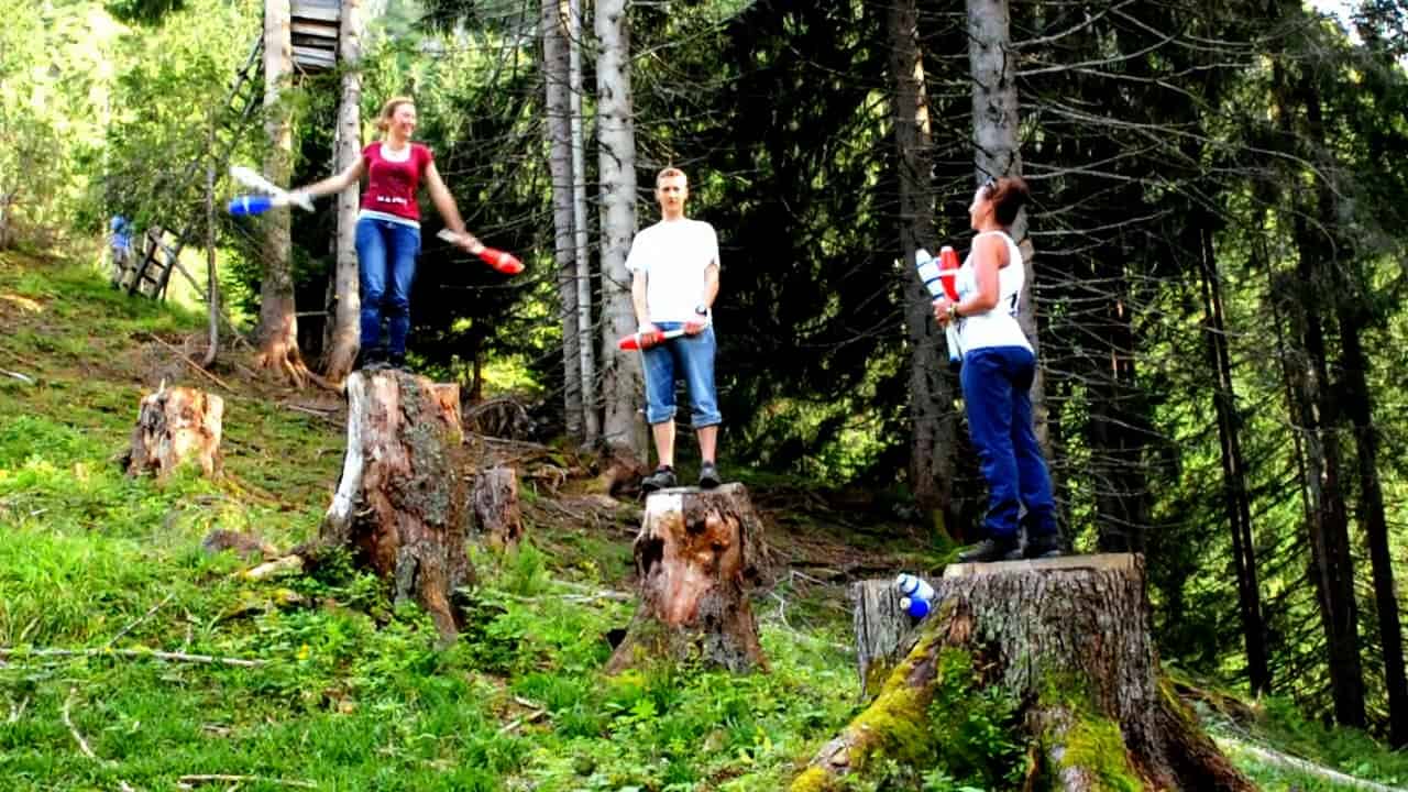People juggling clubs on tree stumps in a forest. Drop Mountain adventure. - Passing Zone