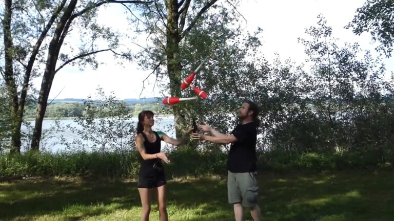 Two people juggling clubs outdoors near a river, possibly related to "Floyd" drinking. - Passing Zone