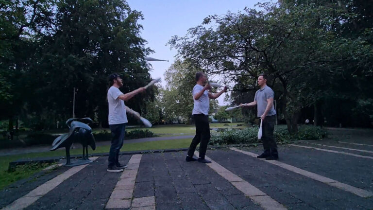 Three men juggling clubs in a park setting. Mini Chopabout No. 8. - Passing Zone