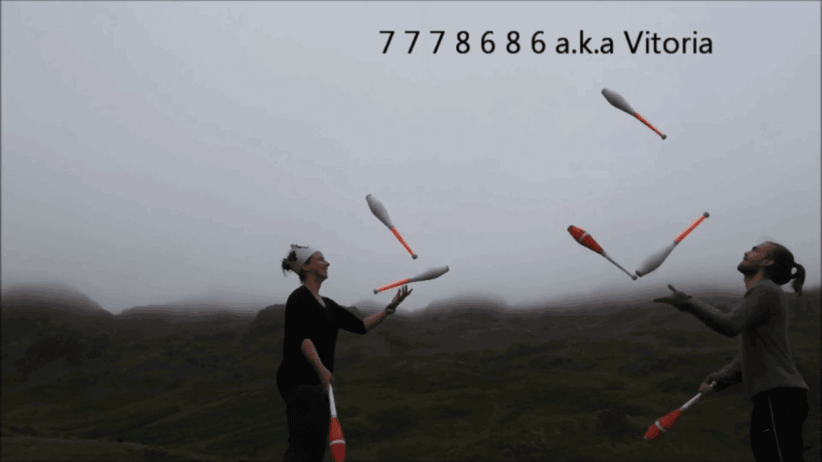 Two jugglers passing clubs, performing a 7 Clubs Passing Workshop routine outdoors with foggy hills in the background. - Passing Zone