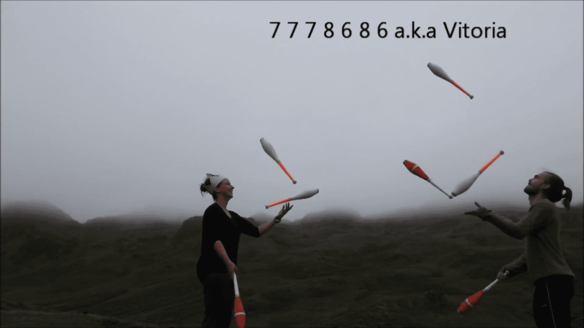Two jugglers passing clubs, performing a 7 Clubs Passing Workshop routine outdoors with foggy hills in the background. - Passing Zone
