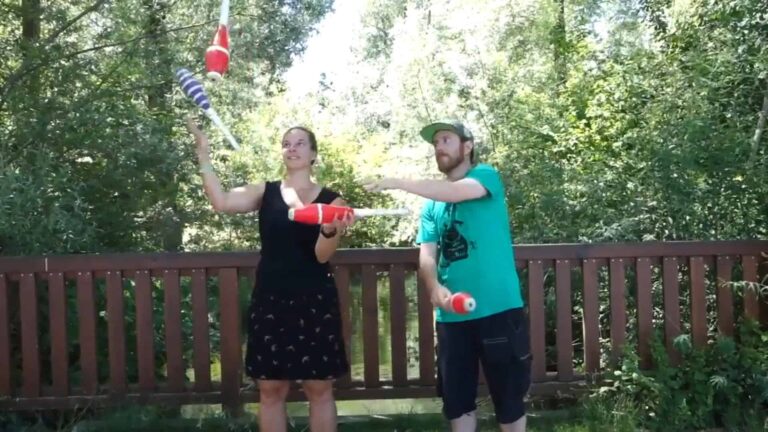 Two people juggling clubs outdoors, with trees in the background. - Passing Zone