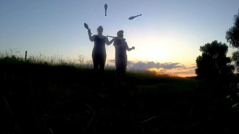 Silhouette of two people juggling clubs at sunset. "Hoschy" event. - Passing Zone
