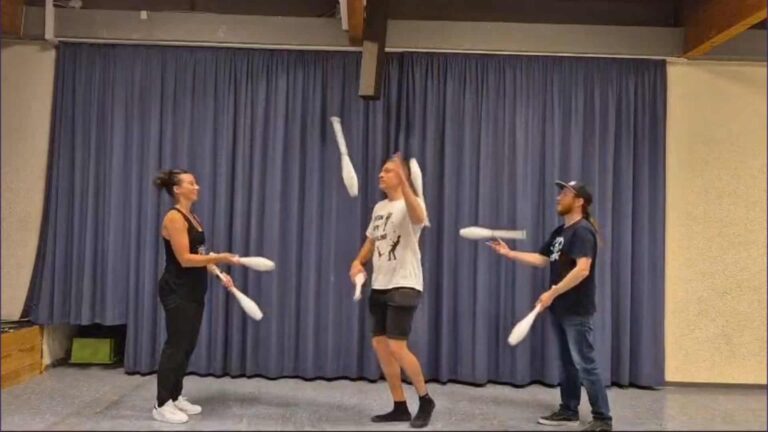 Three people juggling white clubs in a room, performing a juggling routine. - Passing Zone