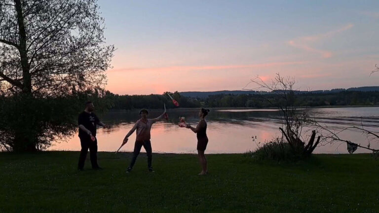 Three people juggling clubs outdoors at sunset by a lake. "Mini Chopabout No. 4 - Susi - Passing Zone